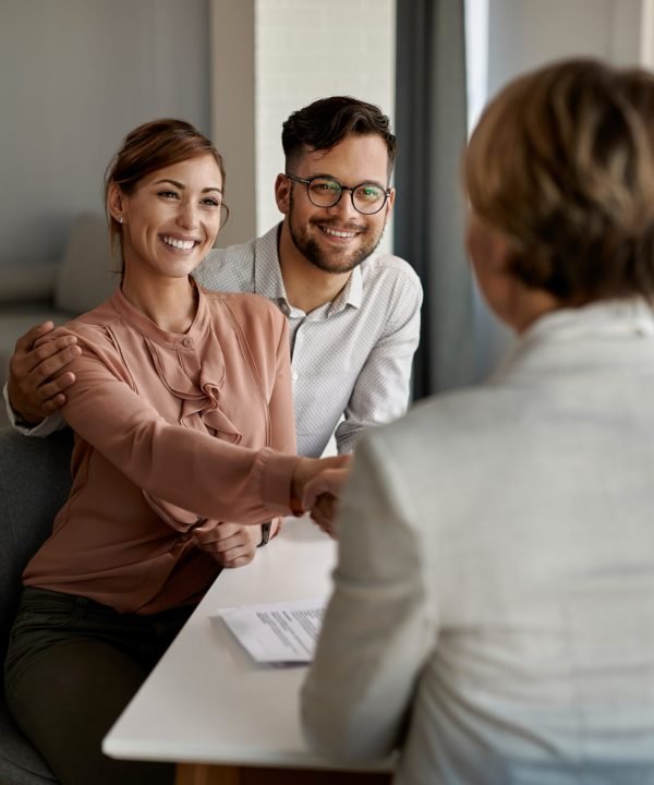 Young happy couple shaking hands with insurance agent during a meeting in the office.